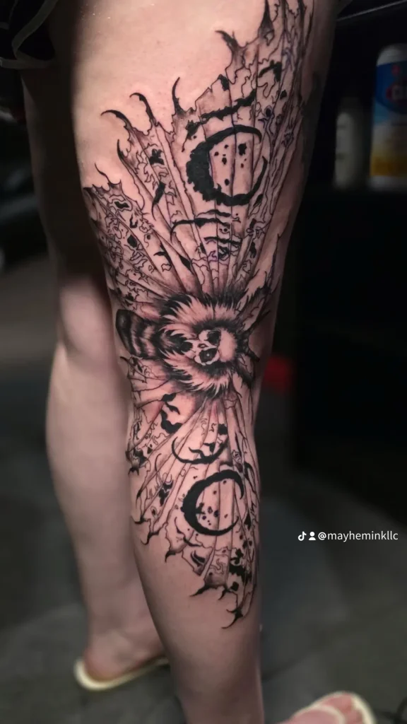 Black and grey dark art tattoo featuring a detailed moth surrounded by sharp, abstract blackwork framing and crescent moon symbols on a person's lower leg.
