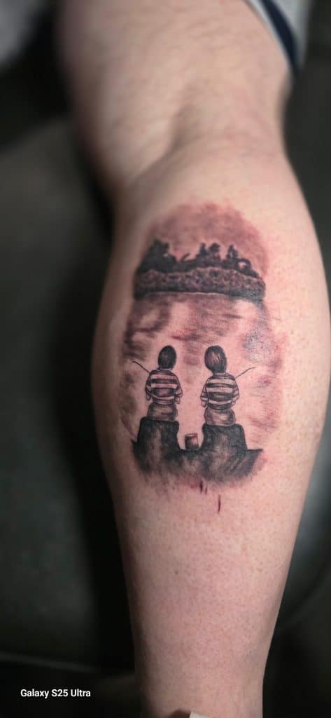 A detailed black and grey tattoo of silhouettes of two kids sitting by a river in a nature scene, custom designed at Mayhem Ink Tattoo in Nashua, NH.