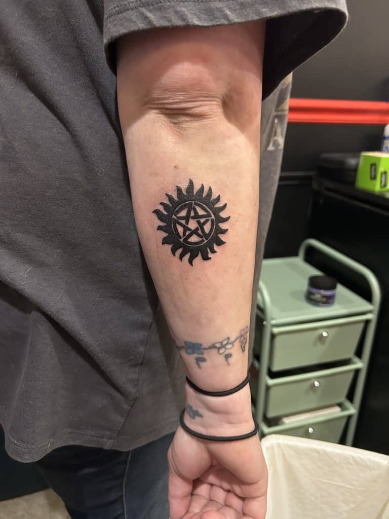 A bold black ink tattoo of a pentagram star surrounded by sun rays on an arm, custom designed at Mayhem Ink Tattoo in Nashua, NH.